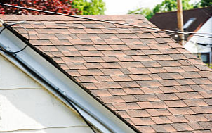 Close-up of a house roof with brown asphalt shingles and a gutter.