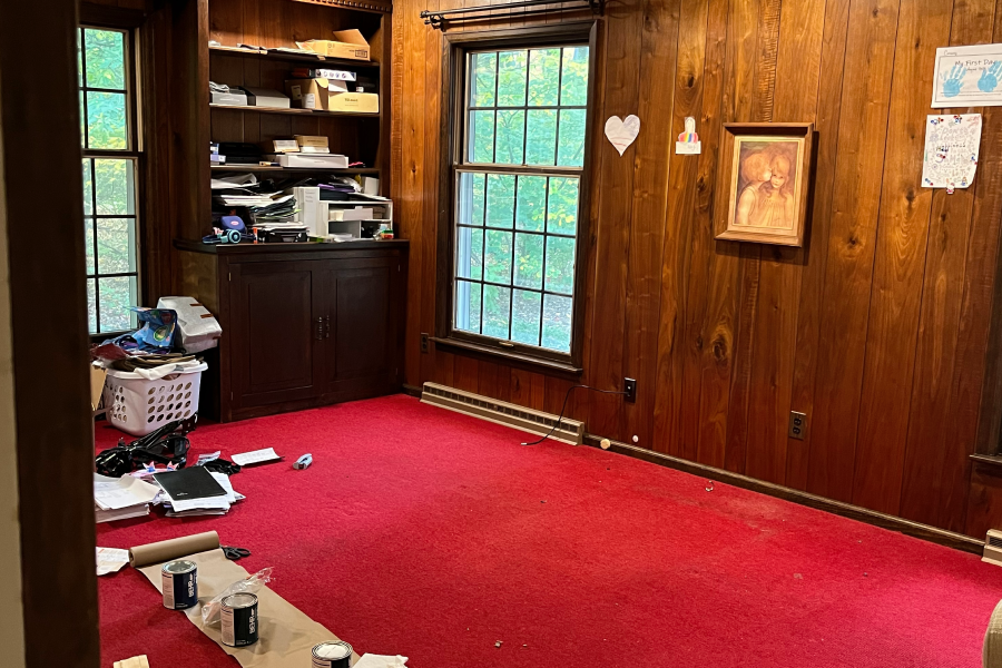 Empty room with red carpet and wooden walls featuring a window and shelves.