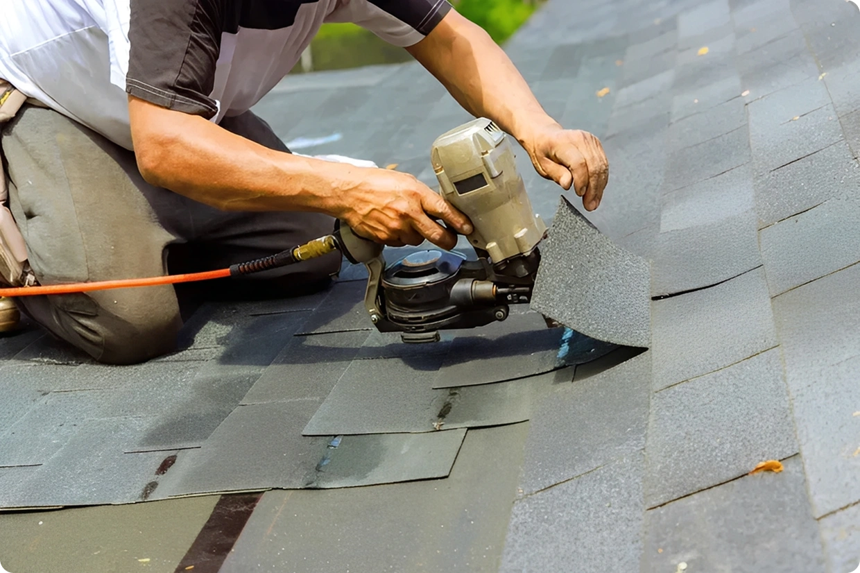 Worker using nail gun on roof shingles